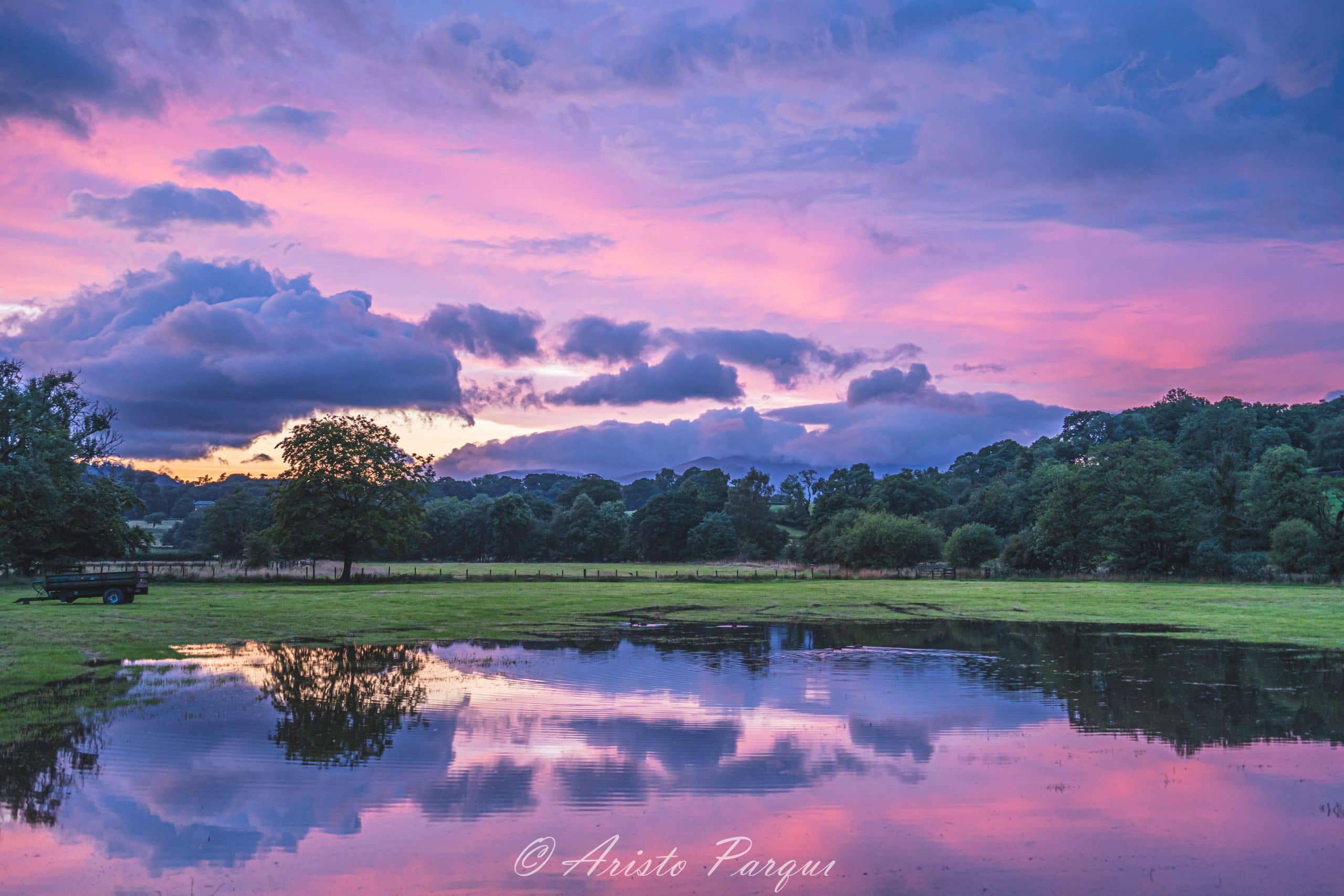 Pink evening skies reflecting in water on a green grass field in Lake District, England.